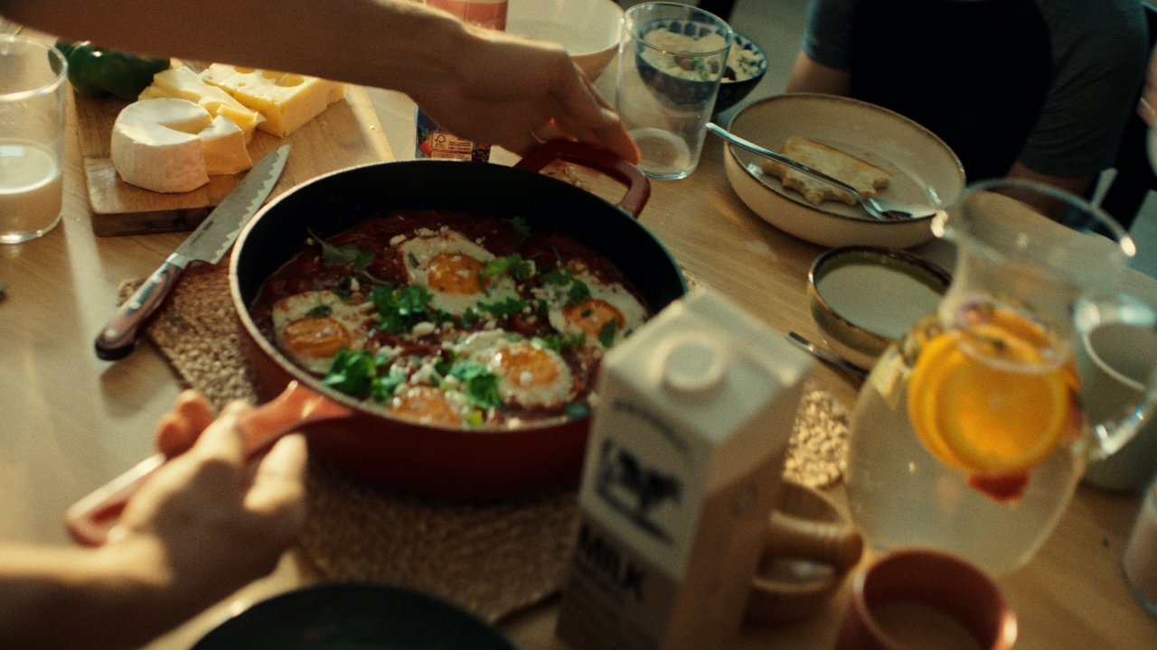 A shared table: a pan of baked eggs, cheese, bread, milk and juice being passed between hands